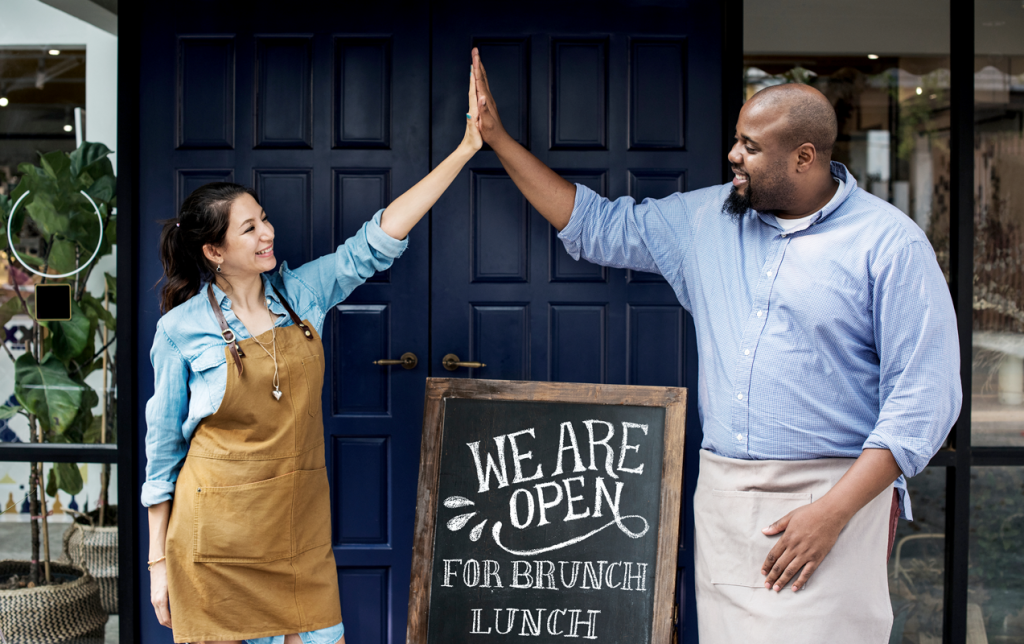 Two small business owners high-fiving in front of their open shop